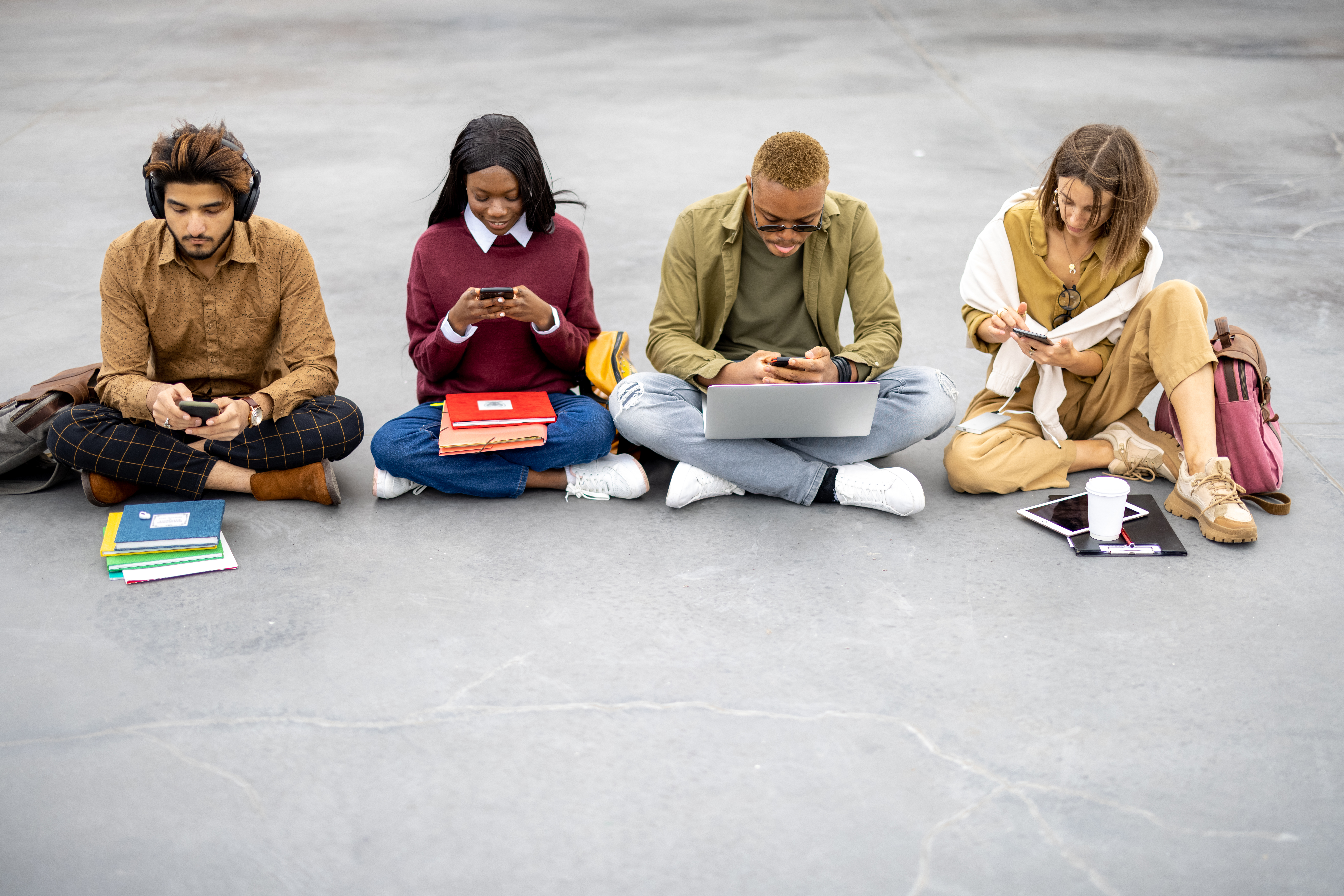 Students with digital devices sitting on asphalt